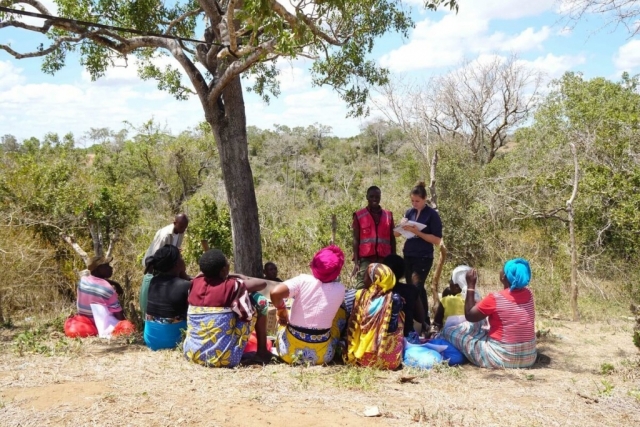 A group of people sit around a tree as they learn new skills from two instructors