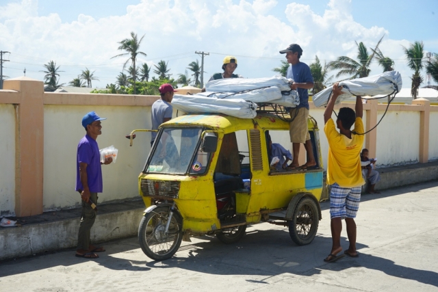 A group of men stack ShelterKits on top of their three-wheel vehicle.