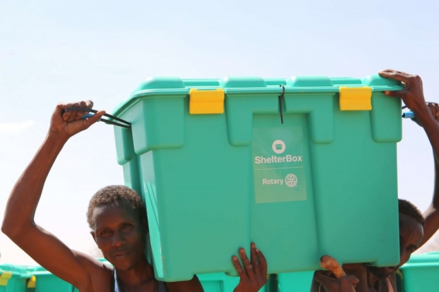 Two men carry a ShelterBox between their shoulders