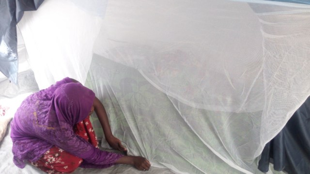 A woman crouches on the floor pulling the edge of a mosquito net to the ground