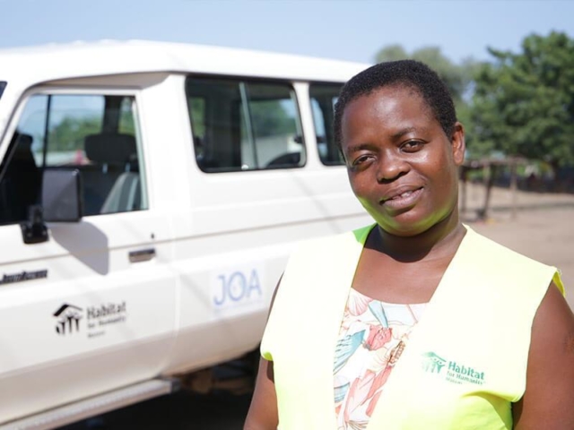 A woman stands next to a truck wearing a Habitat for Humanity vest.