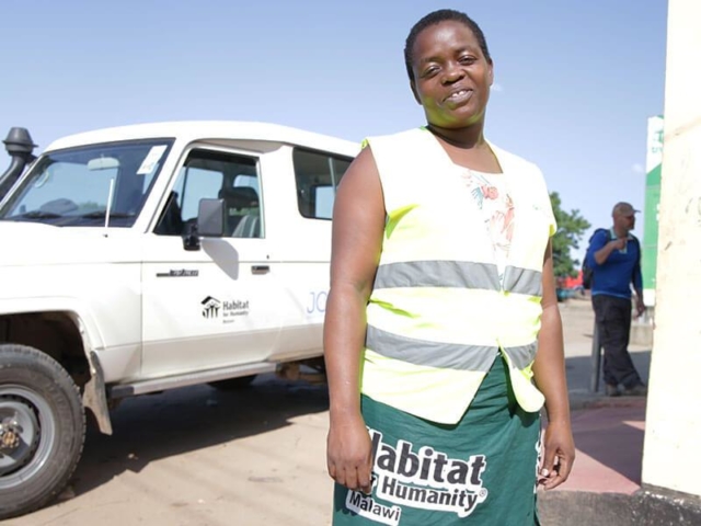 A woman stands next to a truck wearing a Habitat for Humanity vest.