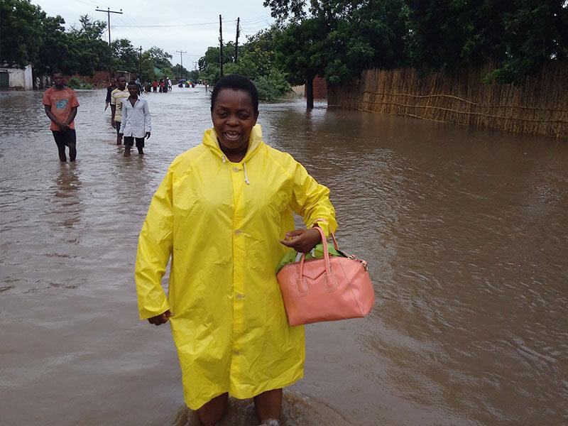 A woman wearing a yellow raincoat stands in water that is up to her knees after flooding in Malawi.