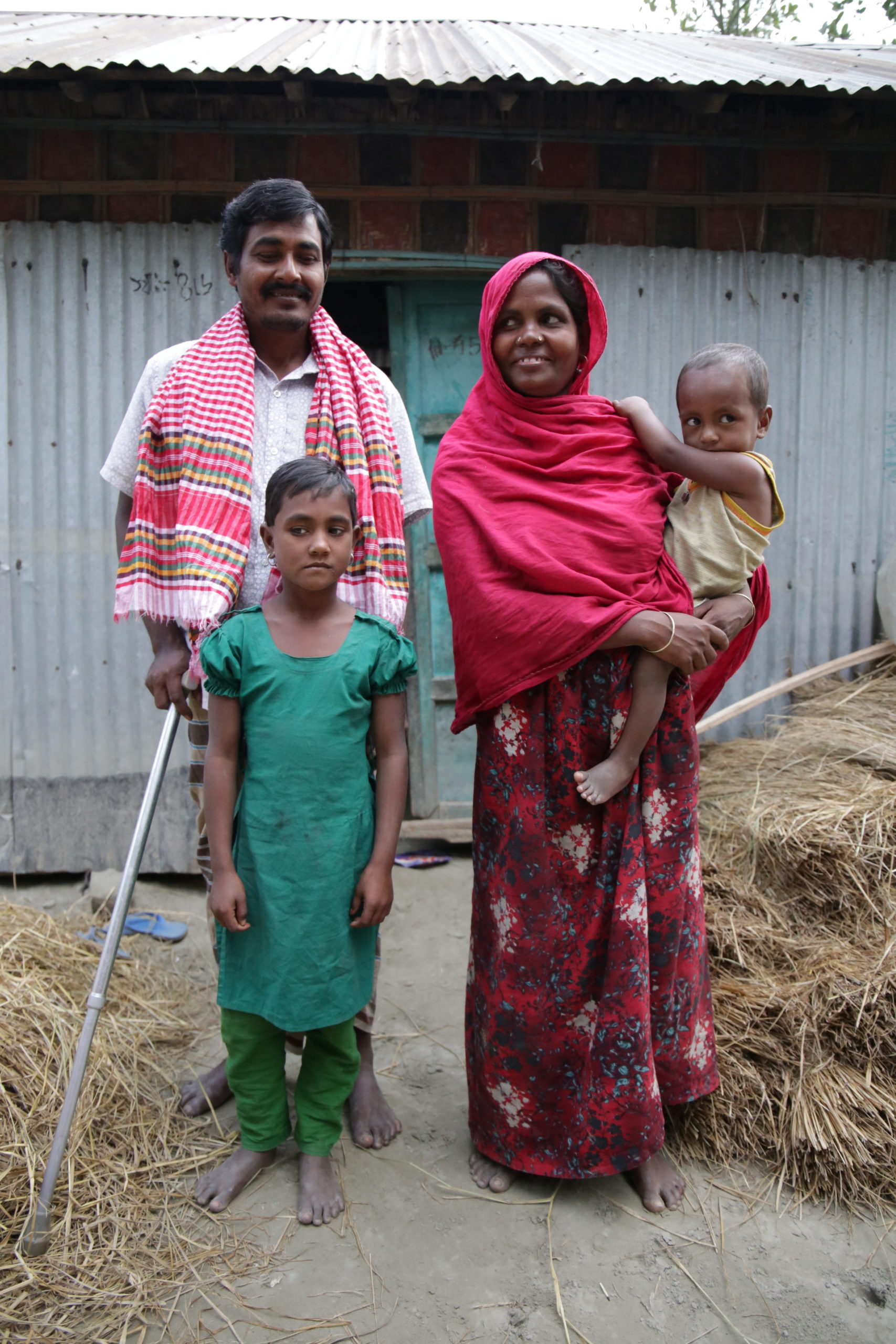 Two adults stand with their two children in front of their shelter.