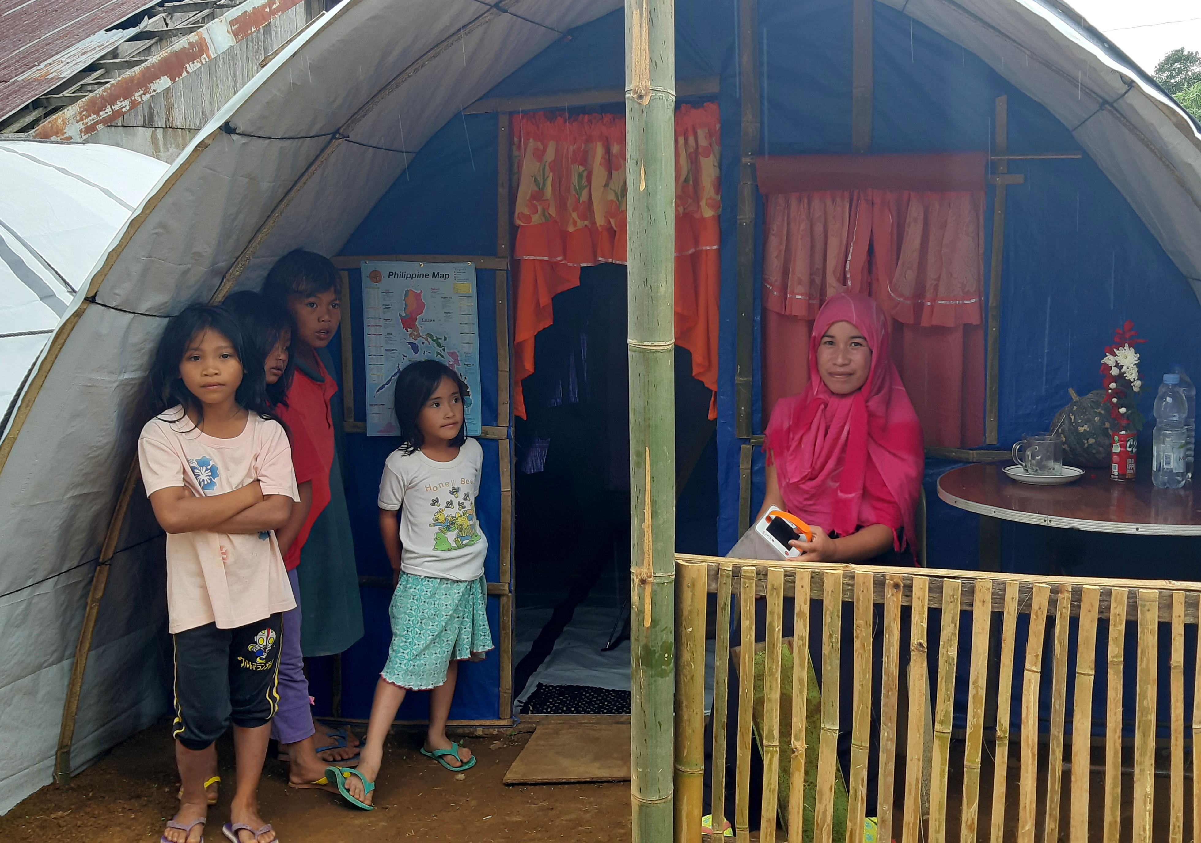 A woman sitting in front of her shelter with four children