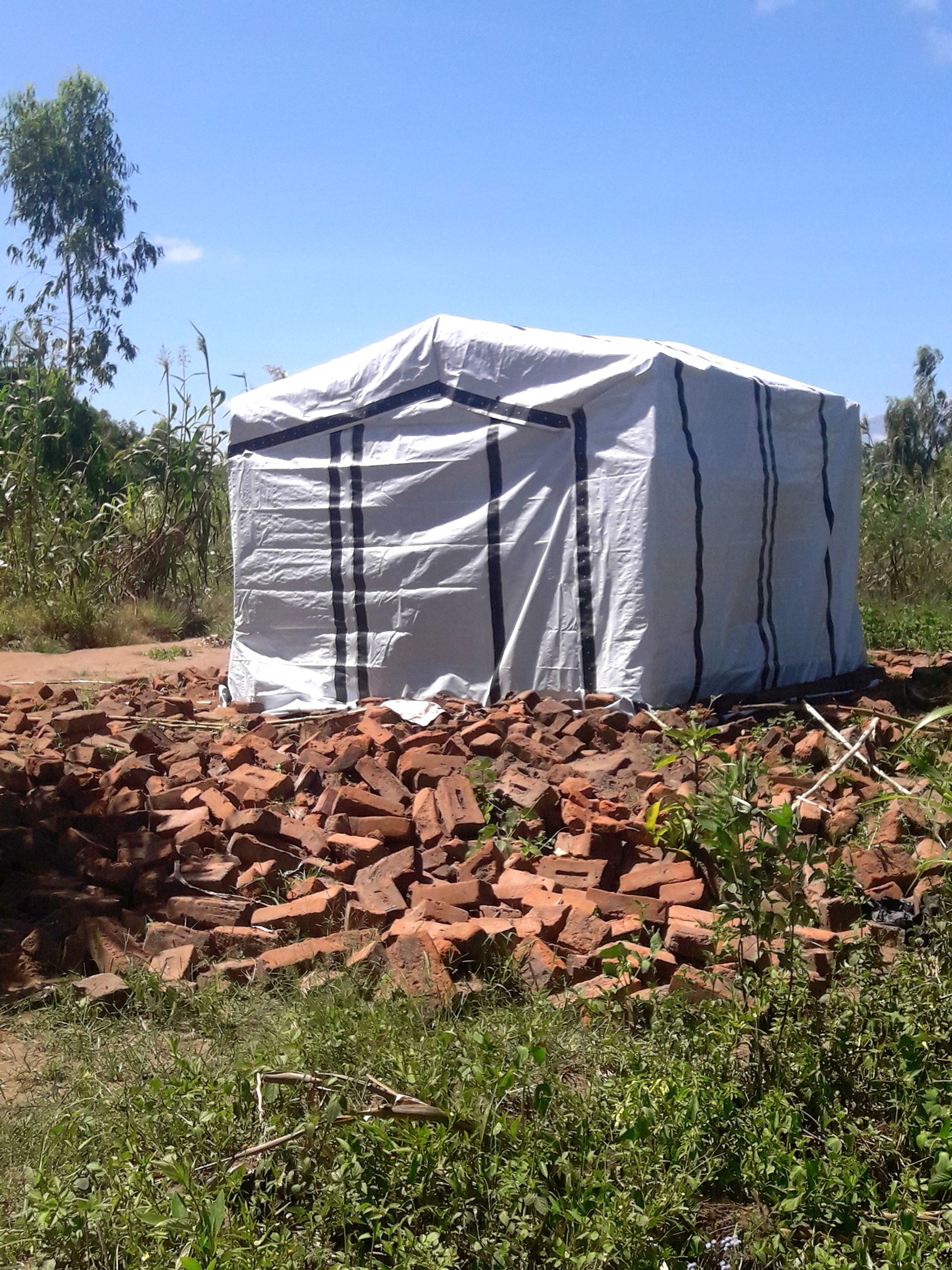 a shelter structure made from ShelterKit materials stands in front of a pile of bricks