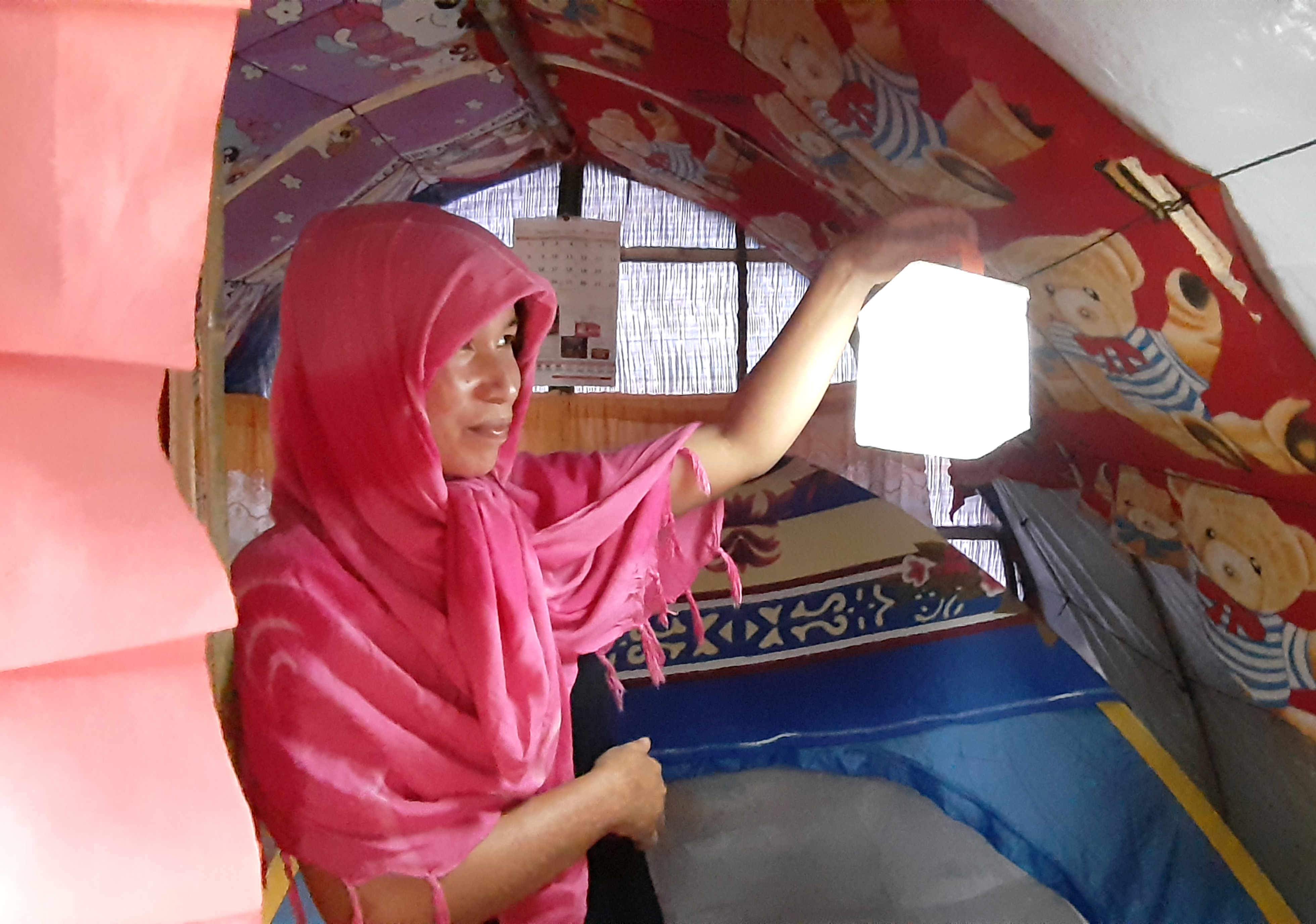 A woman stands in her shelter holding up a solar light that is lit