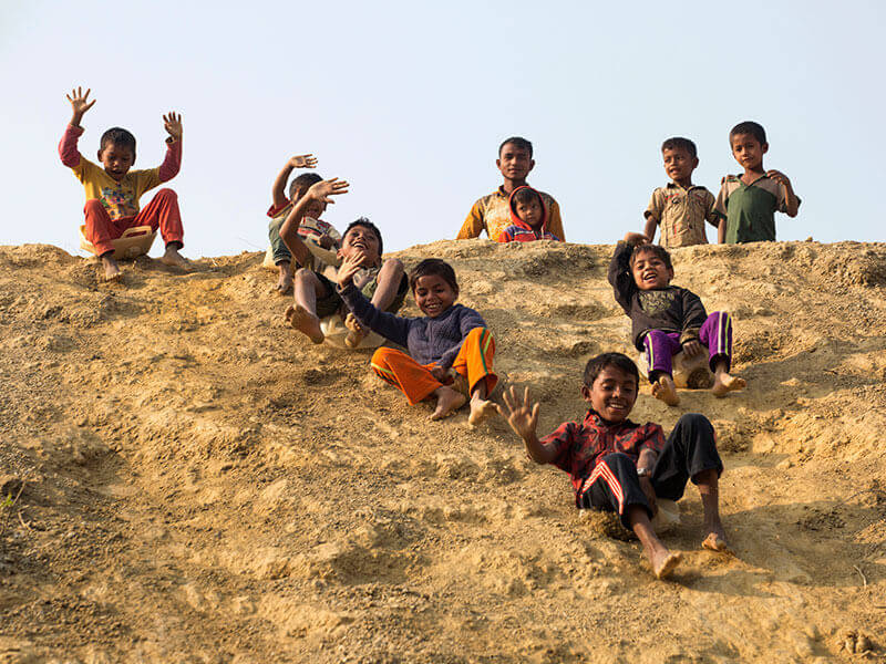 Children sliding down a mud hill on water carriers