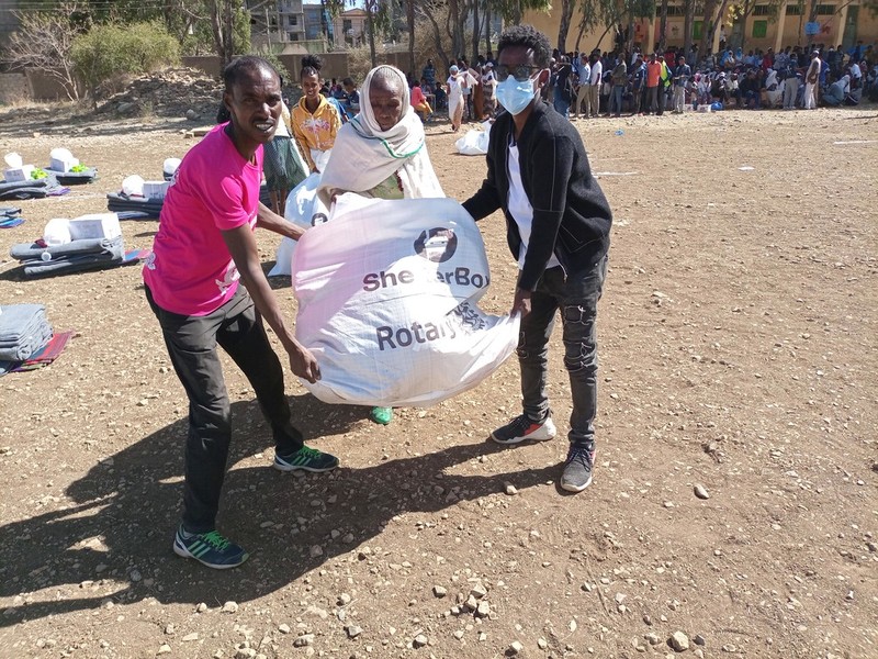 Three people hold a bag of aid that says ShelterBox and Rotary
