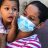 a Honduran woman wearing a medical mask holds her child up