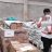 A man wearing a safety vest walking through piles of aid items looking at a sheet of paper