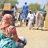 A woman holding aid turned away from the camera, with other people collecting aid in the background.