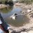 Man stands on the shore next to a lake where his house is submerged