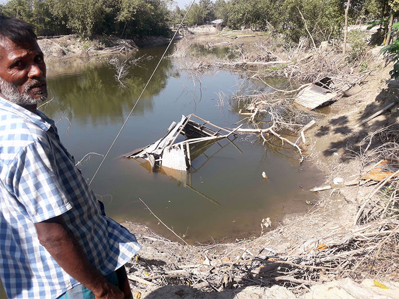 Man stands on the shore next to a lake where his house is submerged