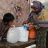 A Pakistani woman uses a ShelterBox water filter to filter water while her child watches.