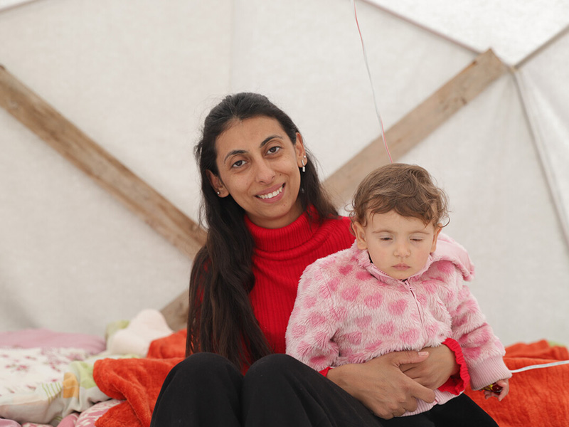 A woman sits holding her child in their tent