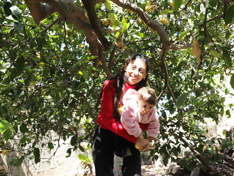 A woman stands under a tree holding her infant daughter